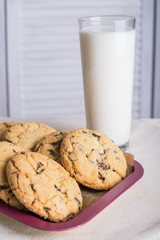 Chocolate biscuits and a glass of milk on a linen towel on a wooden table with a white background. Vintage view. Place for the inscription.