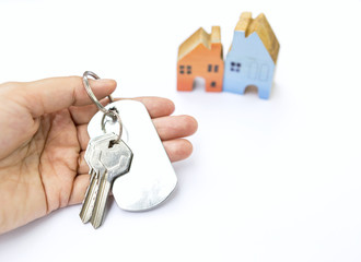 Girl hand holding house key with wooden miniature house on white background