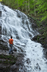 Naklejka na ściany i meble Young man looking at the waterfall in jungles. Man enjoy in wonderful nature in spring