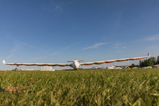 A glider with a protective jacket parked on a grassy airport on a sunny day