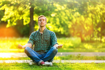 Naklejka na ściany i meble Portrait of serene meditating man with beard in a park at summer golden sunset natural background.