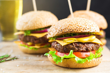 Close-up on a wooden board three beef burgers, with skewers, crispy loaf, lettuce, cheese, tomatoes, cutlets, cucumbers, onions, dark background, delicious, fast food, bright, trendy food, restaurant