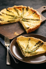 Homemade tart with asparagus and cheese on black background.