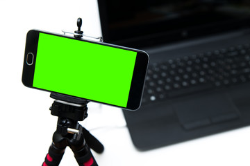 Smart phone on tripod with green key screen record laptop.