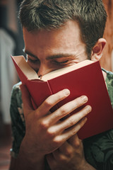 Young man holding a book up to his face, smelling the pages