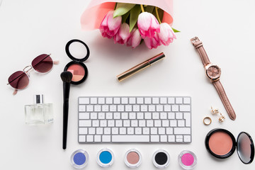 top view of computer keyboard, various cosmetics, accessories and bouquet of pink tulips isolated on white