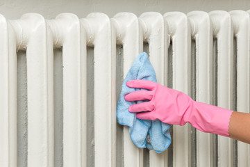 Hand in pink rubber protective glove with rag wiping a heater radiator. Early spring cleaning or...