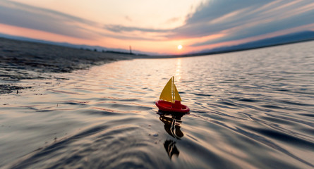 A small children's yellow red boat sails on the sea against the background of the sunrise