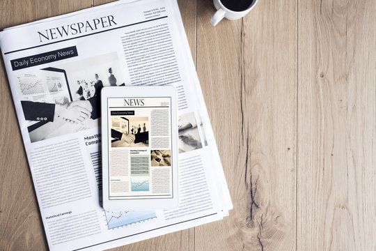 Newspaper with tablet on wooden table