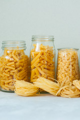 Assortment of different shapes whole grain raw Italian pasta in a glass jar. White stone background. Copy space. Cooking concept.