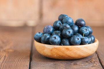 Close up of fresh raw blueberries served in a wooden plate. Wooden background and copy space. Helthy eating and gardening concept.