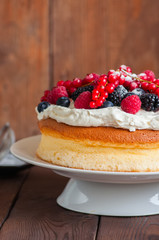 Close up of homemade fluffy Japanese cotton cheesecake decorated with fresh forest berries on a white cake stand on  a wooden background. Copy space.