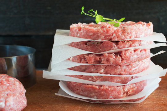 Stack of raw homemade beef burgers on a wooden cutting board with some minsed meat and metal form on a background. Home healthy eating