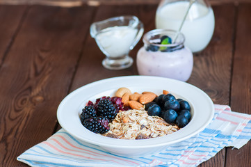 Healthy breakfast concept. Homemade granola with blackberry, dry cranberry, blueberry, almond, yogurt in a jar, sour cream and milk on a wooden background. Close up and copy space.