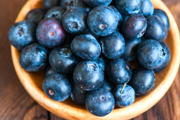 Fototapeta premium Close up of fresh raw blueberries served in a wooden plate. Wooden background and copy space. Helthy eating and gardening concept.