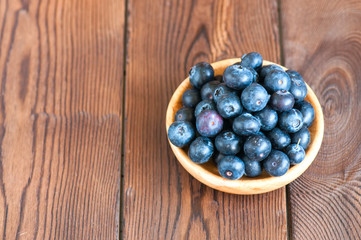 Close up of fresh raw blueberries served in a wooden plate. Wooden background and copy space. Helthy eating and gardening concept.