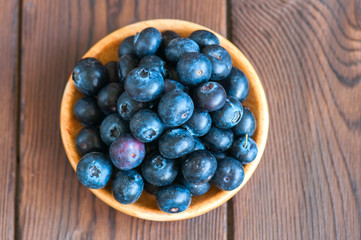 Close up of fresh raw blueberries served in a wooden plate. Wooden background and copy space. Helthy eating and gardening concept.