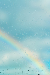 Water drops on a window with the rainbow in the background © KariDesign