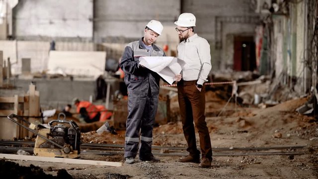 The engineer shows the customer in a protective helmet the estimate of a new building in order to amend its reconstruction