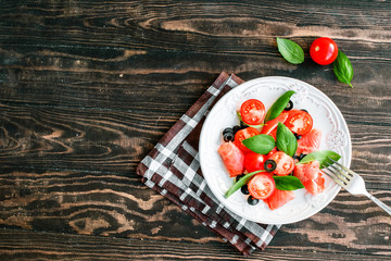 salad with salmon, basil, tomatoes and olives in bowl on napkin and wooden table