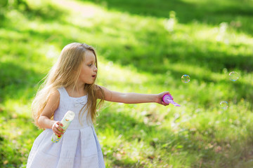 Obraz premium Cute little girl is blowing a soap bubbles. Summer time.