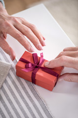 cropped shot of man presenting gift in box with ribbon to his wife