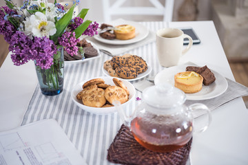 lilac flowers with tea and various pastry with cookies on tabletop