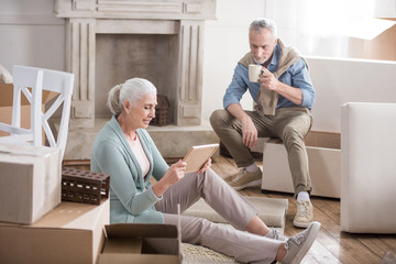senior woman looking at photo frame with husband drinking coffee near by