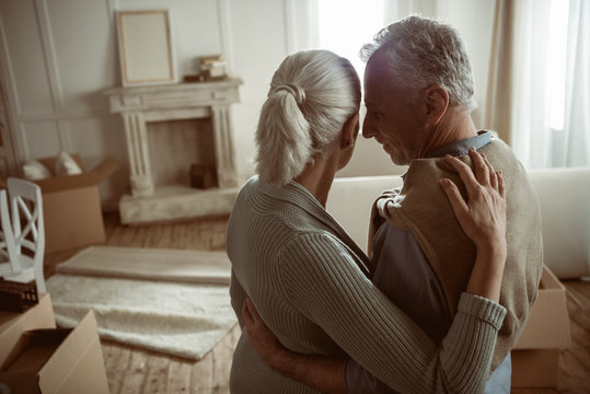 tender senior husband and wife embracing and looking at their home, moving out concept