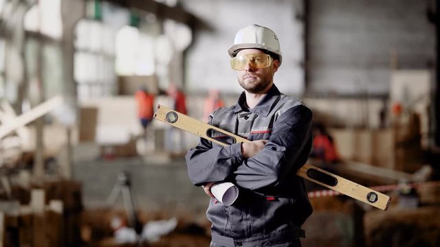 An adult engineer in a helmet holds in his hands a spirit level for measuring the degree of deviation of the surface from the horizontal plane