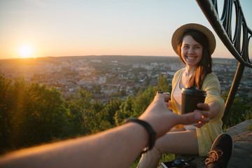 Female giving coffee to man while they sitting on the hill on sunrise