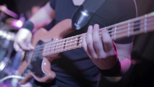 Man bass guitarist playing electrical guitar on concert stage 