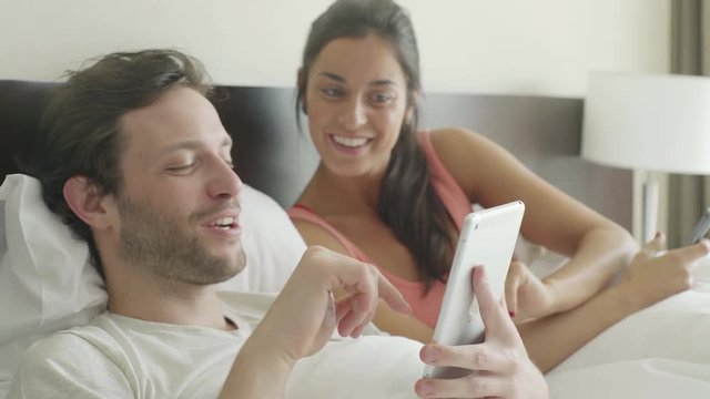 Couple relaxing in bed chatting while using personal wireless devices
