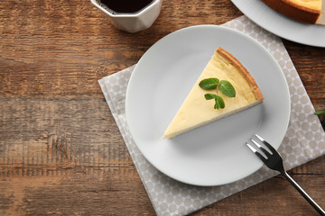 Plate with piece of tasty cheesecake on wooden table
