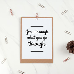 Inspirational motivational quote "Grow through what you go through" on sheet of note paper and paper clips background.