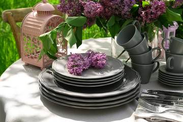 Set of dishware and lilac flowers decoration on table outdoors