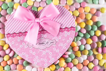 Pink heart box with bow above colorful round candies