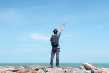 Traveler standing and raising his hand on the rock starring at the sea