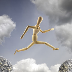 Wooden mannequin is jumping over the abyss at cloudy sky background