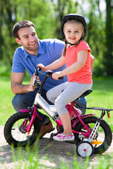Obraz premium Girl learning to ride a bicycle with father 