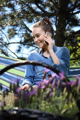 Relaks w ogrodzie. Młoda atrakcyjna kobieta wypoczywa na hamaku w ogrodzie rozmawiając przez telefon