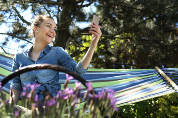 Chilout w ogrodzie.Młoda atrakcyjna kobieta wypoczywa na hamaku w ogrodzie rozmawiając przez telefon - obrazy, fototapety, plakaty