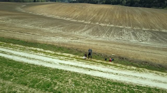 Film crew launches drone at the field. Man operating the copter, woman shoots on camera. Aerial view of the countryside.