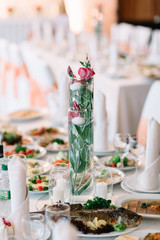 Tall vase with candles and flowers stands on the dinner table