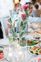 Tall vases with candles and flowers stand in the center of dinner table
