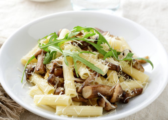 Pasta with mushrooms and arugula in white bowl