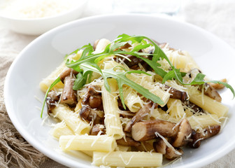 Pasta with mushrooms, arugula and parmesan in white bowl