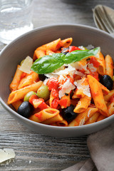 Penne Pasta in tomato sauce with olive and cheese on a wooden table