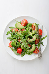 Fresh Salad with avocado, tomatoes and arugula on white wooden background