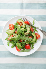 Green Avocado Salad with cherry tomatoes and arugula on a stripy background